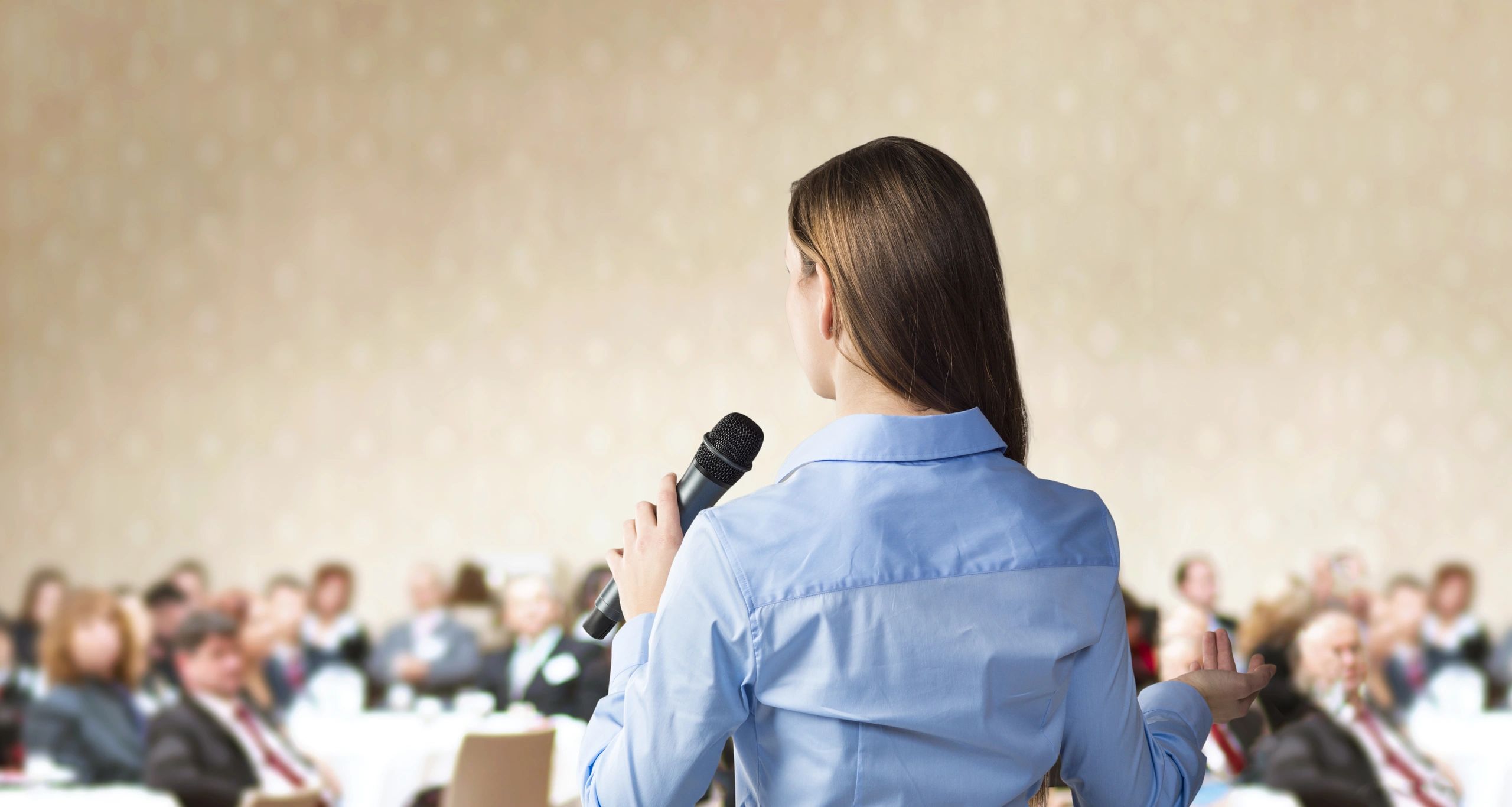 Woman speaking to an audience with a microphone.
