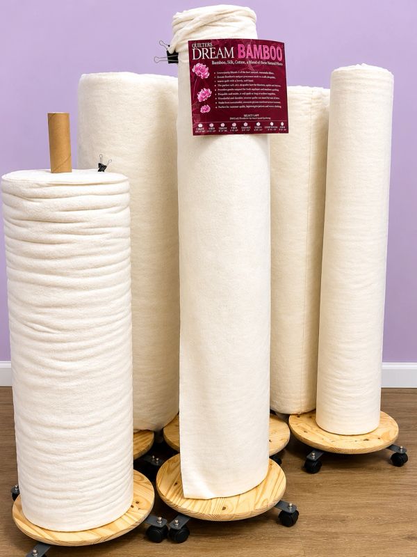 Large rolls of soft quilting bamboo fabric on wooden stands with wheels.