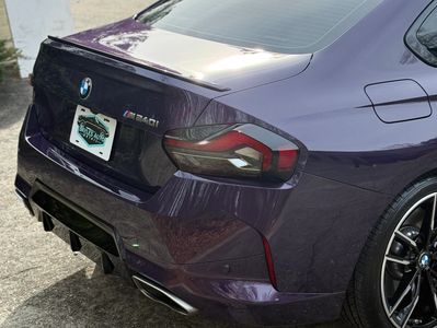 Rear view of a purple BMW M340i with tinted taillights and dual exhaust.