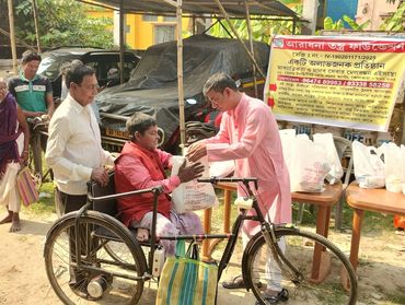 A man in pink distributes food to a person in a wheelchair during a community event.