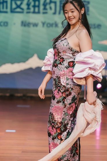 Young woman in a floral dress posing on stage with a smile.