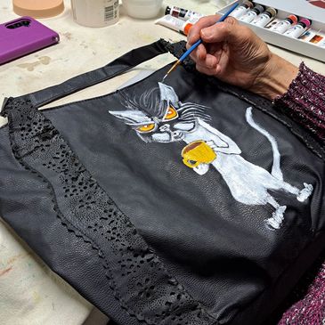 Hand painting a cartoon cat on a black leather bag.