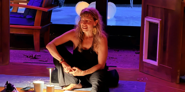 Woman sitting on floor under warm purple lighting, relaxed and smiling.