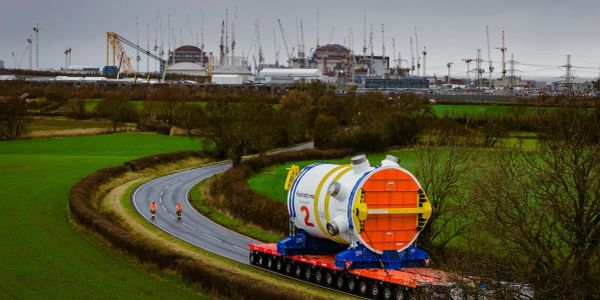 A large industrial component transported on a curved road through green fields.