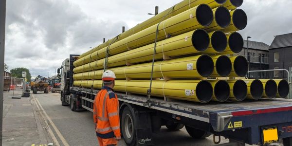 Worker observing a truck loaded with yellow pipes on a cloudy day.