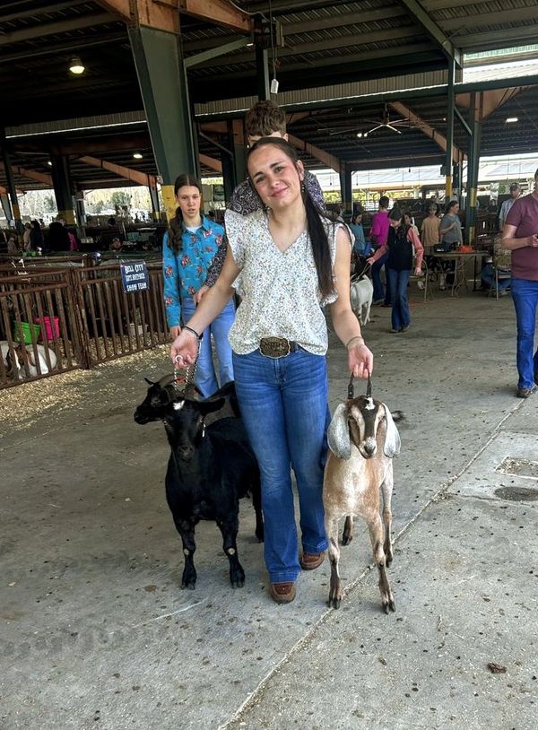A young woman holding two goats in a livestock pavilion.