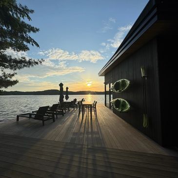 Sunset at a lakeside dock with kayaks and chairs.