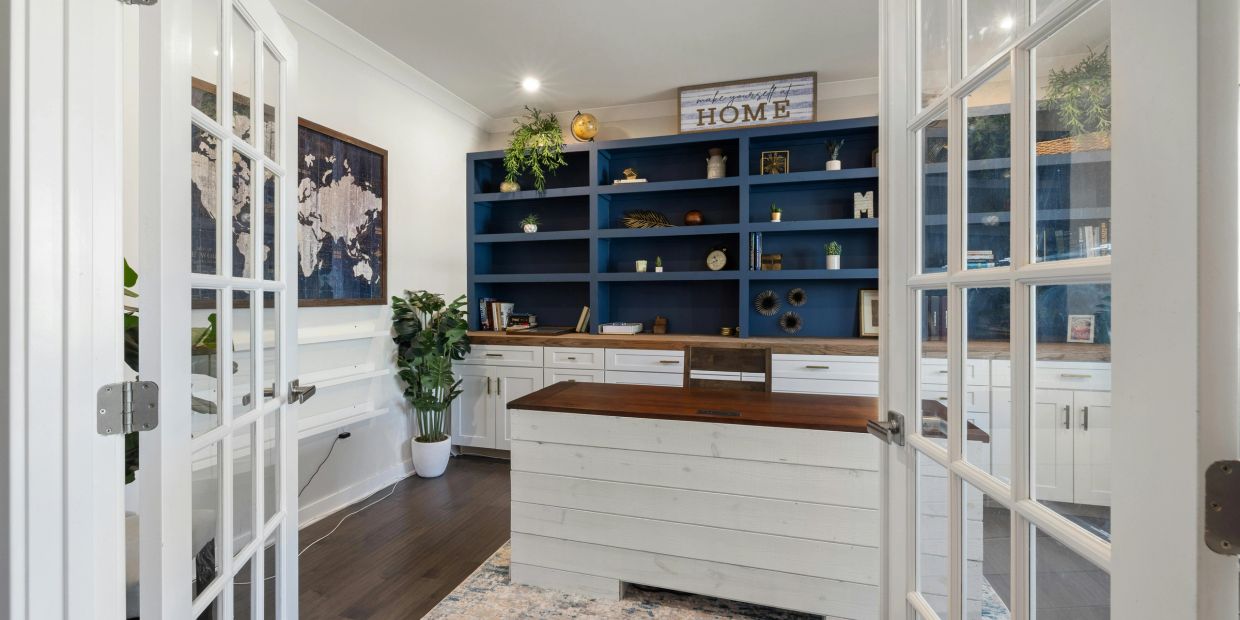 Bright home office with white furniture, blue shelves, and indoor plants.