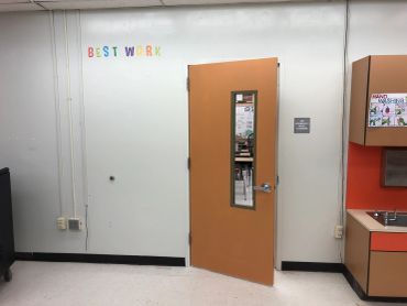 Classroom door slightly open with colorful 'Best Work' letters on the wall.