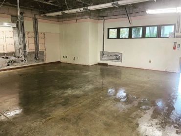 Empty industrial room with polished concrete floor and overhead lighting.