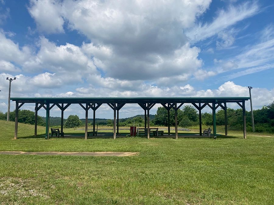 Open pavilion with benches under a partly cloudy sky in a grassy field.