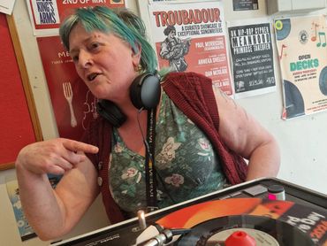 A woman with headphones and colorful hair DJing at a music venue.