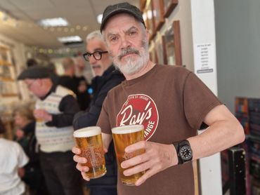 Man holding two pints of beer indoors at a social event.