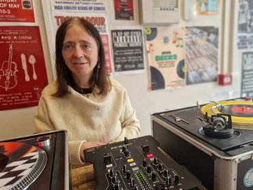 A woman operates DJ equipment in a room with posters on the wall.