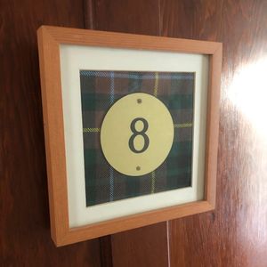 Framed number 8 on a plaid background hanging on a wooden wall.