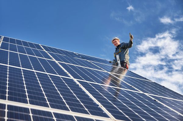 Solar panels and a smiling solar panel installer with thumbs up. Preventing power outages.