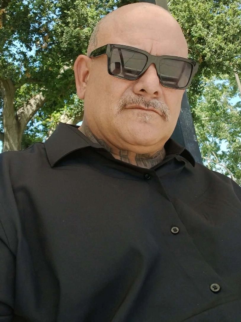 Man wearing sunglasses and a black shirt sitting outside.