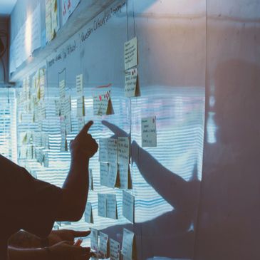 Person pointing at sticky notes on a whiteboard during brainstorming.