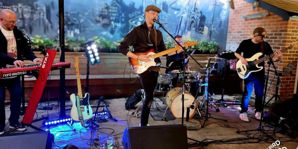 A band performs live with guitar, keyboard, bass, and drums in an intimate venue.