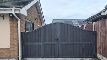 Arched metal framed driveway gates with dark grey composite board infill. steelwork galvanised and p