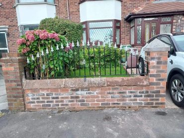 arched railing sat on a garden wall between pillars. the railing has gold finials & decorative baske