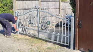 finalising the installation of a pair of ornate galvanised gates with a floral centre piece on each