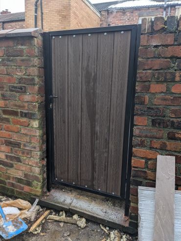 single gate between brick walls, black steel frame with brown composite