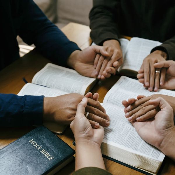 People holding hands and reading the Bible together.