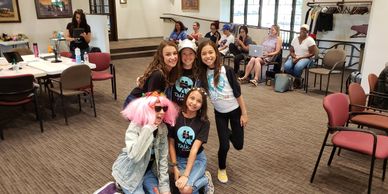 A group of our students, in a class, huddled together and smiling in their talk to the camera Tees.