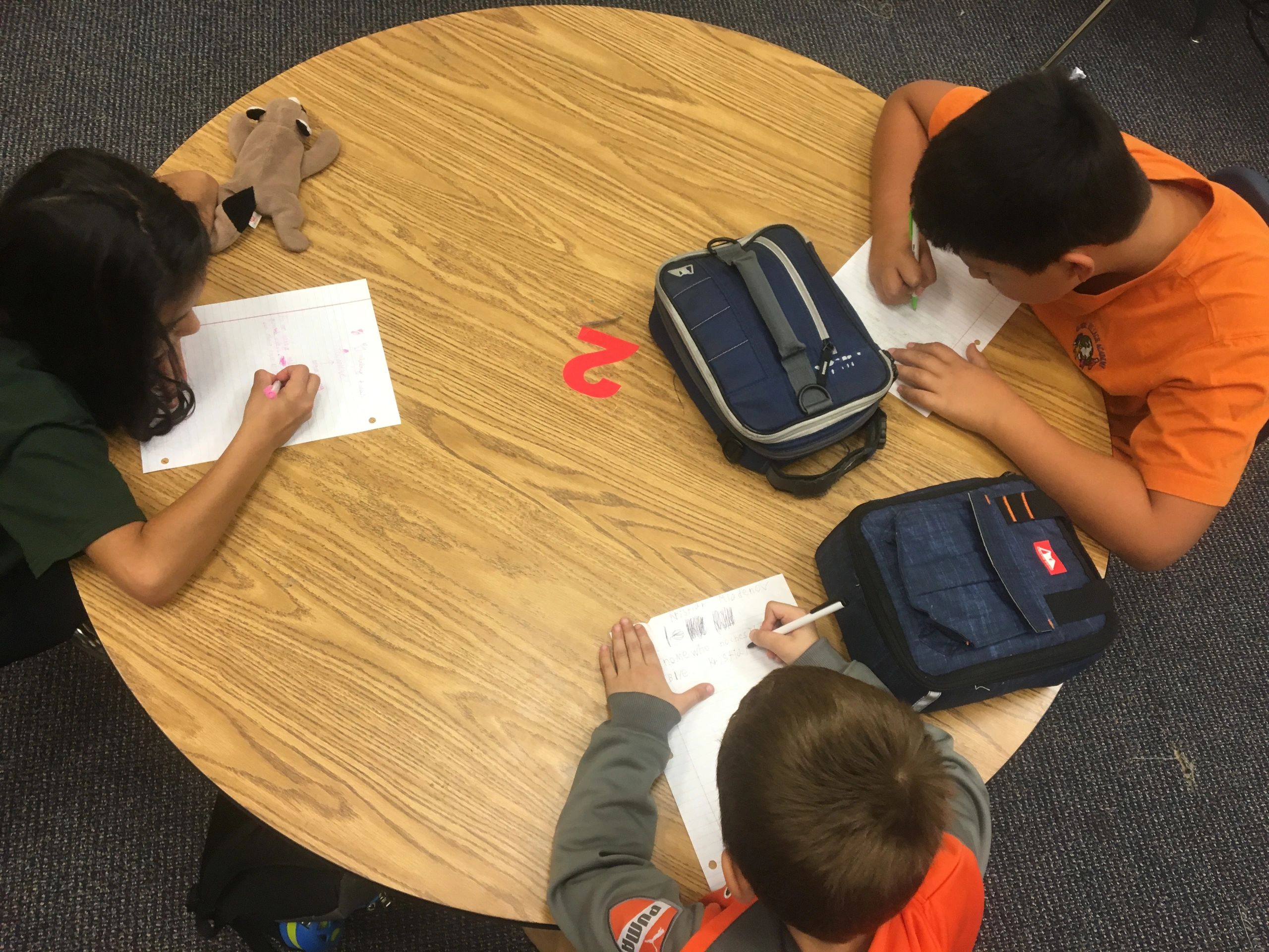 Overhead photo of three kids drawing scenes at a table. two have their lunchboxes.