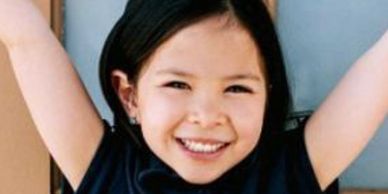 A headshot of a young Talk to the Camera brand ambassadors-smiling and holding up her arms-Yay!