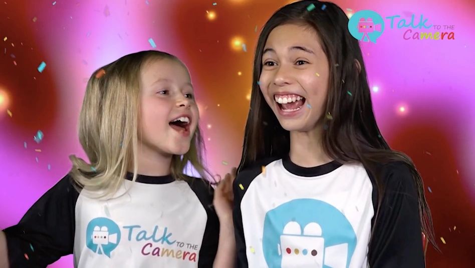 A photo of two young actors, on-set, laughing, wearing talk to the camera tees.