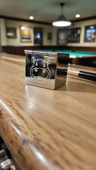 Shiny metal cube with a hippo face on a pool table.
