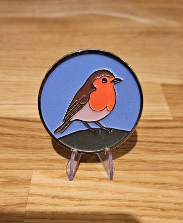 Enamel pin of a robin bird on a blue background.