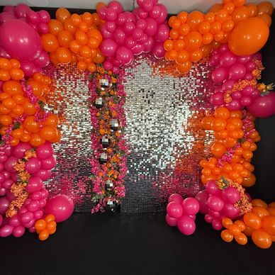 Vibrant balloon arch with pink and orange balloons surrounding a shiny silver backdrop.