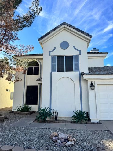 Two-story white house with blue accents and desert landscaping under a blue sky.