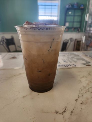 Iced coffee with foam and chocolate on top in a clear plastic cup.