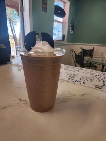 Oreo milkshake topped with whipped cream in a plastic cup on a café counter.