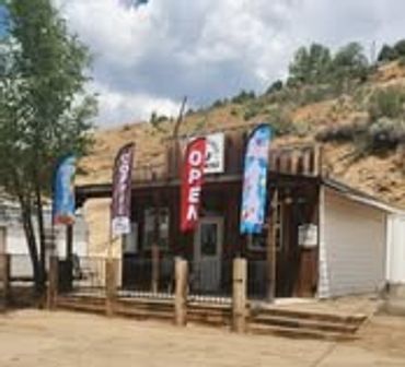 Rustic wooden shop with colorful 'Open' and 'Ice' flags on a sunny day.