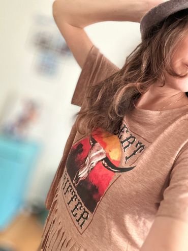 Person wearing a brown shirt with a bull skull graphic and text.