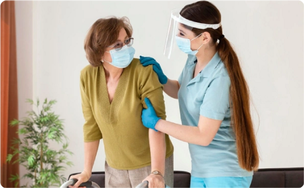 Healthcare worker assisting an elderly woman with a walker.
