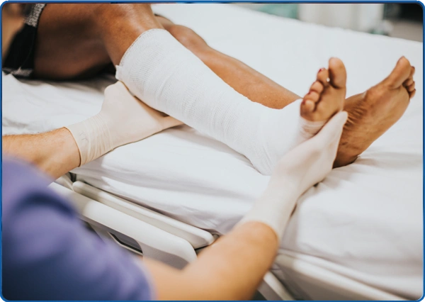 Medical professional examining a patient's bandaged leg in a hospital bed.