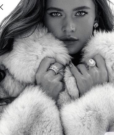 Black and white close-up of a woman in a fur coat with striking eyes and jewelry.