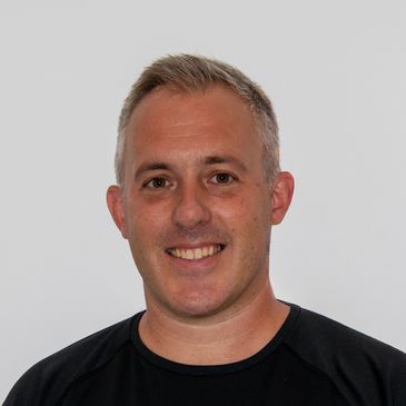 Smiling man with short gray hair wearing a black shirt against a plain background.