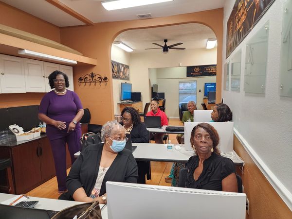 A group of adults in a computer class with one instructor standing.