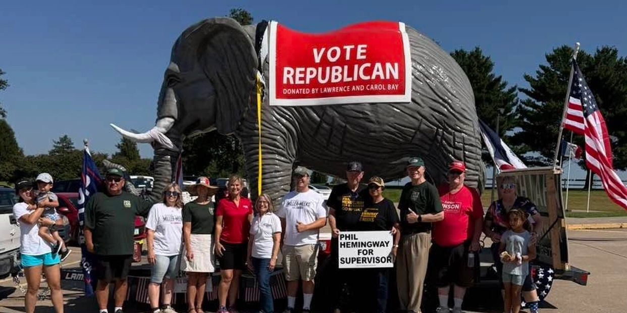 Group posing with large elephant and political signs for Republican vote.