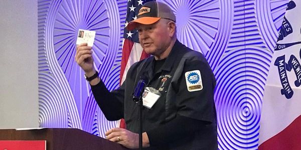 Man speaking at podium holding an ID card.