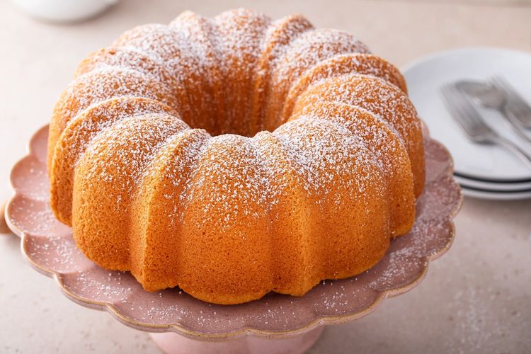 Golden Bundt cake dusted with powdered sugar on a pink cake stand.