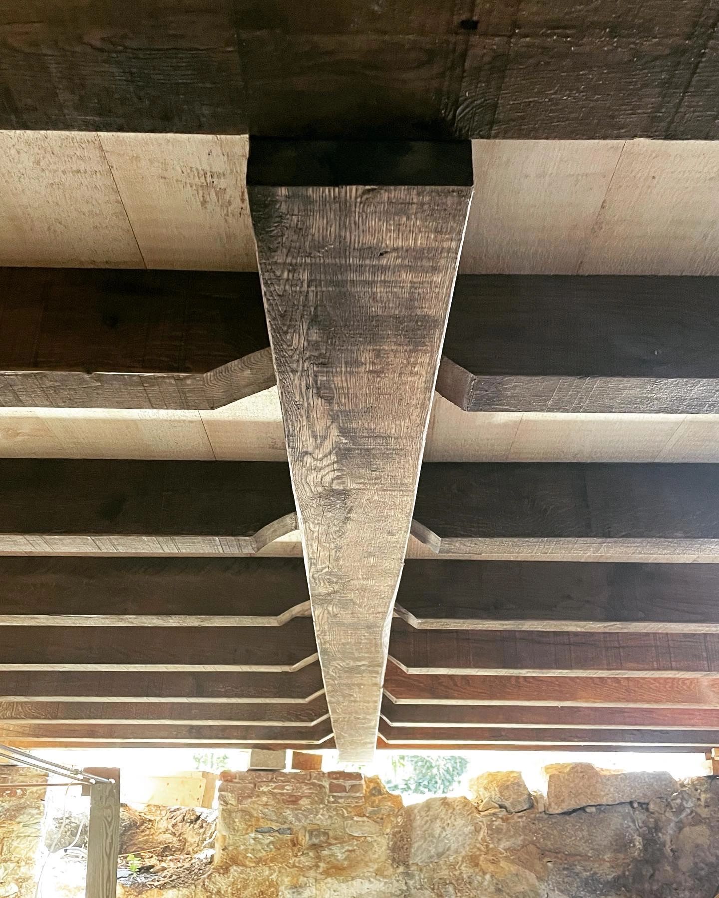 View of rustic wooden beams supporting a ceiling over stone walls.