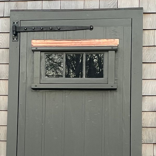 Gray wooden door with small window and shingled exterior wall.